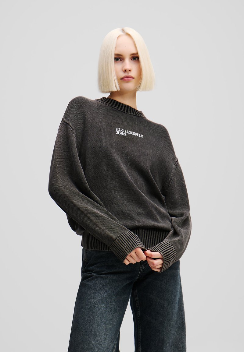 Tamsiai pilkas per didelis megztinis su banguotu kaklu ir rankogaliais, papuoštas balta "KARL LAGERFELD JEANS" logo priekyje.