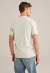 Krémové tričko s krátkým rukávem vyrobené z měkké, hladké látky. Jednoduchý design s kulatým výstřihem a žádnými viditelnými vzory nebo akcenty.