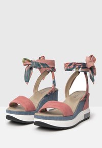 Sandales à talons compensés en suède rose avec une plateforme bleue, liens en tissu floral autour de la cheville et conception ouverte à l'avant. Semelle blanche plate pour le confort.