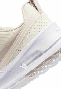 Lichtbeige atletische schoen met een gestructureerde bovenkant, perforaties voor ventilatie en een contrasterende witte zool met een zichtbare luchtunit.