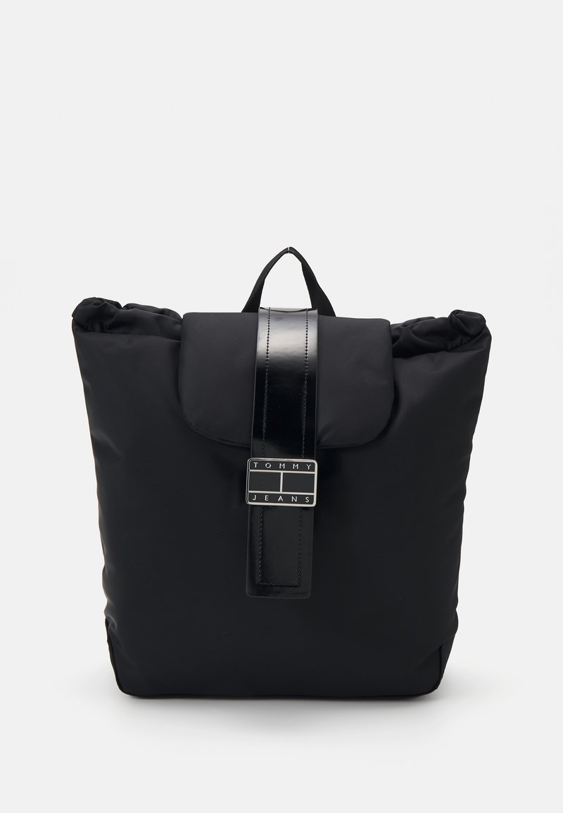 Sac à dos noir avec une poignée supérieure, une fermeture à rabat et une sangle brillante avec une boucle rectangulaire arborant le logo Tommy Jeans.