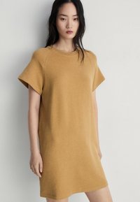 Rochie tip tricou de culoare galben muștar, cu mâneci scurte, croială lejeră și un material moale, texturat. Design simplu, fără modele sau accente.