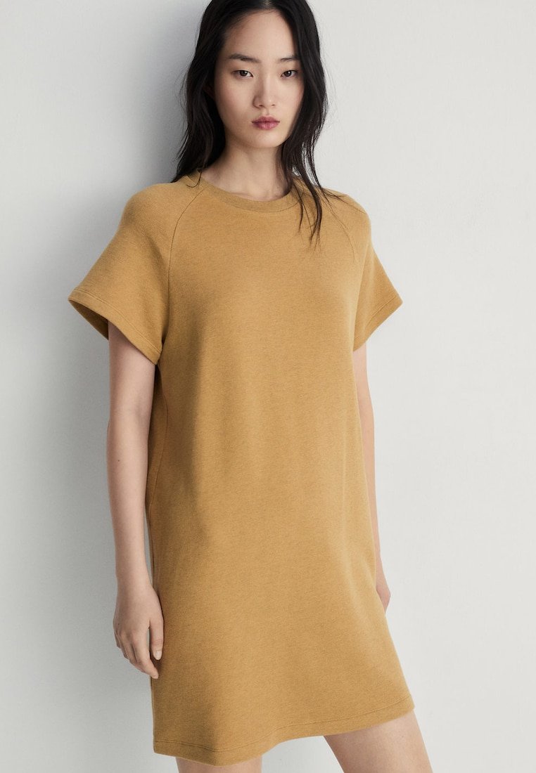 Rochie tip tricou de culoare galben muștar, cu mâneci scurte, croială lejeră și un material moale, texturat. Design simplu, fără modele sau accente.