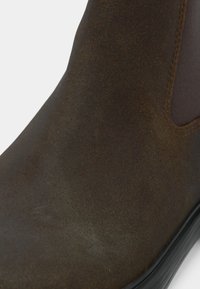 Rjava usnjena gležnjarica z gladko teksturo, elastičnimi bočnimi paneli in črnim gumijastim podplatom, s poudarkom na okroglem dizajnu prstov.