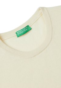 Crème kleurige gebreide trui met een geribbelde ronde hals. Bevat een groen label met de tekst "United Colors of Benetton" bij de kraag.