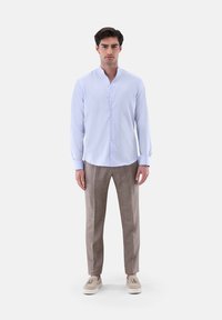 Hellblaues langärmliges Hemd mit Stehkragen, kombiniert mit beige strukturierten Hosen und beigen Schuhen, die ein einfaches Knopfdesign aufweisen.