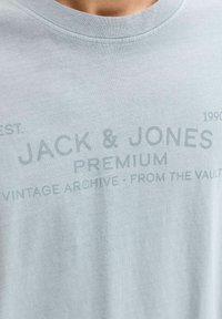 Hellblaues Baumwoll-T-Shirt mit Rundhalsausschnitt und gedrucktem Branding in dunkleren Farbtönen. Die Stofftextur wirkt weich und glatt.