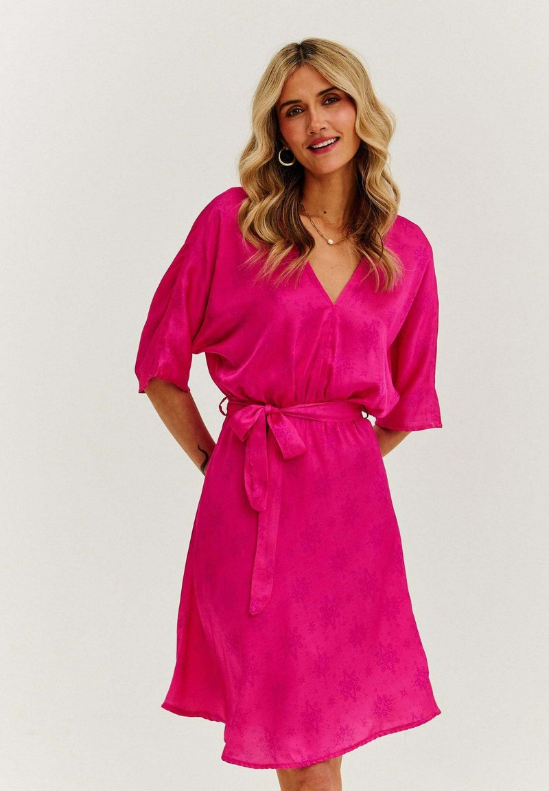 Fuchsia šaty s výstrihom do V, krátkymi rukávmi a opaskom v páse. Mäkká tkanina s jemnými kvetinovými vzormi, jemne rozšírený spodný lem.