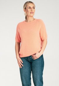 Różowy sweter z krótkim rękawem, okrągłym dekoltem, miękką fakturą i luźnym krojem, zestawiony z niebieskimi dżinsami z wysokim stanem.