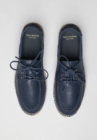 Zapatos de cuero azul marino con diseño de cordones. Costuras de color claro a lo largo de la suela, tacón plano y marca mínima en la plantilla.