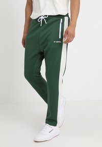 Gröna joggers med vita sidostråk, tillverkade av slätt tyg, med dragsko i midjan och en dragkedjeficka på framsidan.