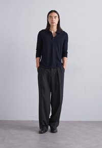 Schwarzes Langarm-Polohemd mit Kragen, kombiniert mit lockeren schwarzen Hosen. Der Stoff wirkt weich mit einer glatten Textur.