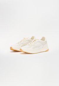 Kerged beige sneakerid, mis on valmistatud võrgust ja sünteetilisest materjalist, millel on tekstuuriga pealis, seotud nööridega ja kummise põhja ning kummi tallaga.