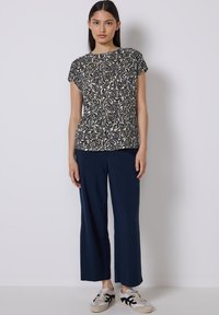 Marineblaue weit geschnittene Hosen mit einer texturierten Oberfläche, kombiniert mit einem kurzärmeligen Oberteil mit einem cremefarbenen und dunkel gemusterten Blumenmuster.