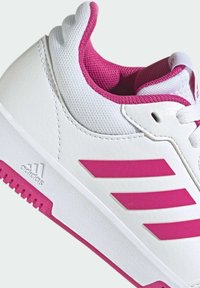 Baskets blanches avec des accents roses, comprenant un dessus texturé, un système de laçage et trois bandes roses proéminentes sur le côté.
