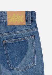 Jeans laget av denim med et brunt lærmerke som har gul dekorativ tekst. Stoffet er blått med en lett falmet tekstur og synlige sømmer.