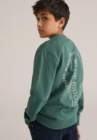 Hanorac verde din material moale, cu guler rotund și manșete ribbate, având grafica textului alb imprimată pe spate.