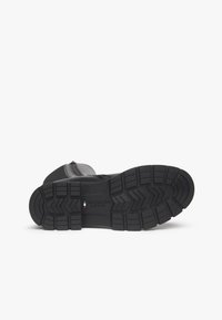 Botte en cuir noir avec une semelle en caoutchouc texturé, dotée de profonds crampons et d'un logo en relief. Conçue pour la durabilité et l'adhérence.