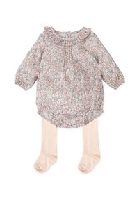 Blusa floral con cuello rizado en rosa pastel, con mangas largas y un dobladillo redondeado. Combinada con medias ligeras de color beige.