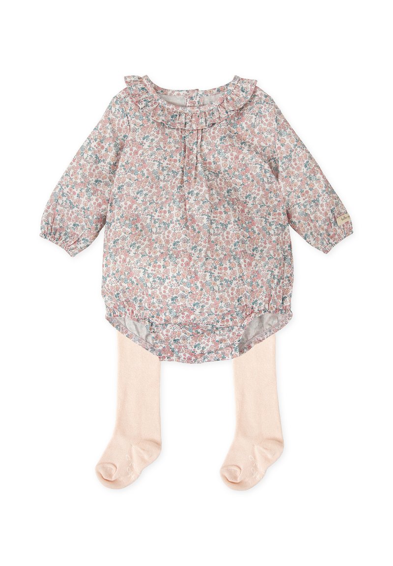 Blusa floral con cuello rizado en rosa pastel, con mangas largas y un dobladillo redondeado. Combinada con medias ligeras de color beige.