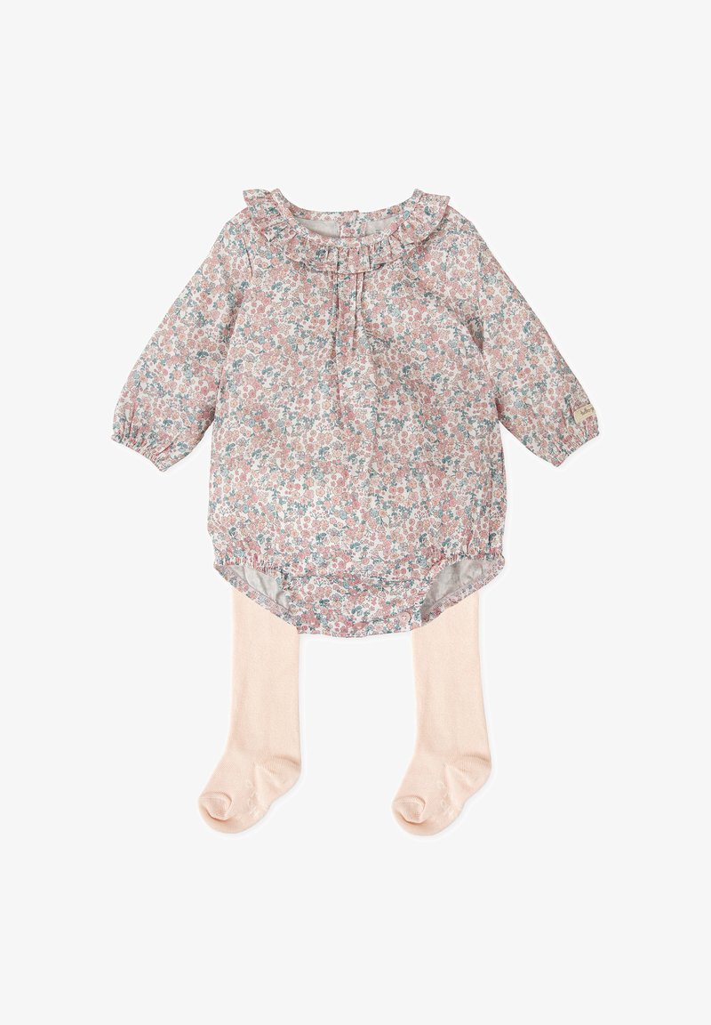 Blusa floral con cuello rizado en rosa pastel, con mangas largas y un dobladillo redondeado. Combinada con medias ligeras de color beige.