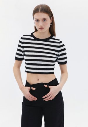 Sort og hvid stribet cropped sweater med korte ærmer og rund halsudskæringer, parret med højtaljede sorte bukser.