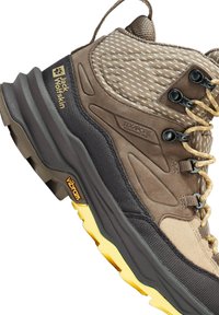 Scarpa da trekking marrone e beige con suola Vibram nera e gialla, ganci per lacci e logo Jack Wolfskin sul pannello laterale del tallone.