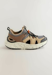 Chaussures de sport avec un mélange de matériaux gris, marron et beige, dotées d'une semelle texturée et mouchetée, ainsi que de lacets élastiques pour un maintien sécurisé.