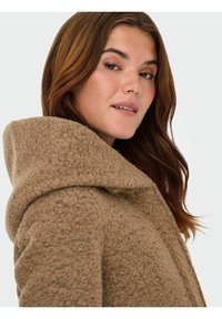 Bruine wolmix jas met een gestructureerde afwerking, grote capuchon en een comfortabele pasvorm, met zichtbare stiksels.