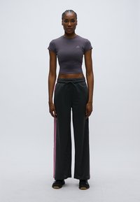 Sötétszürke rövid felső és fekete, bő szárú nadrág rózsaszín oldalsávokkal. A nadrág texturált anyagból készült, húzózsinóros derékrésszel és laza szabással.