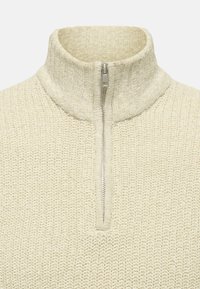 Gebreide kwart-rits trui in off-white met een gestructureerd patroon. Beschikt over een hoge kraag en een metalen ritssluiting.