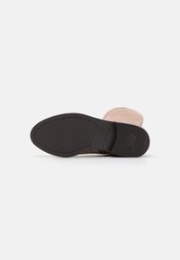 Semelle en caoutchouc noire d'une botte beige clair, talon plat avec grip rayé et texte "ANTI GLISSE" visible sur la zone du talon.