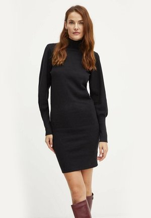 Abito in maglia nera con collo alto e maniche lunghe. Forma aderente che si estende fino a metà coscia. Texture liscia con dettagli a coste.