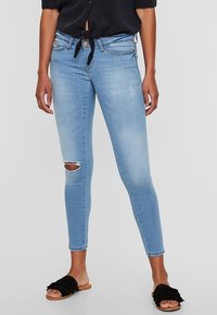 Jeans skinny de color azul claro con un detalle de rodilla rasgada, hechos de denim, con una cintura de altura media y un cinturón de tela atado con un lazo.