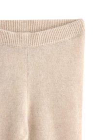 Pantaloni beige a vita alta in maglia con una cintura elastica a coste, che mostrano un tessuto morbido e strutturato e un dettaglio di cucitura centrale.