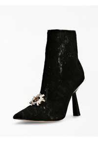 Stivaletto in pizzo nero con punta affilata, tacco a stiletto e un dettaglio decorativo con una spilla a forma di teschio e strass.