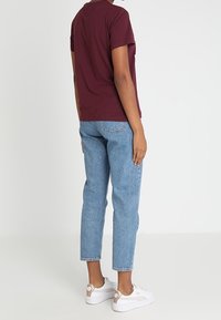 Burgundy short-sleeve t-shirt paired with light blue tapered jeans and white sneakers with rose gold accents. Smooth fabric, casual fit.