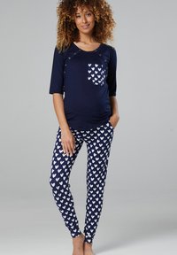 Maternity loungewear set featuring a navy top with snap details and a heart-patterned pocket, paired with matching pajama pants covered in heart prints.