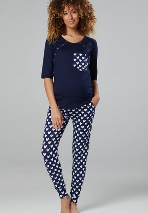 Maternity loungewear set featuring a navy top with snap details and a heart-patterned pocket, paired with matching pajama pants covered in heart prints.