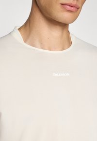White, short-sleeved athletic shirt with a round neckline. Features subtle texture and a small "Salomon" logo in white on the front.
