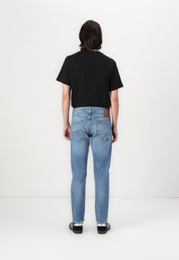 Black short-sleeve t-shirt paired with light blue denim jeans. Jeans feature a brown leather patch and two back pockets.