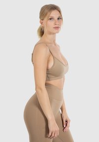 Mellembrun sportsbh med tynde stropper og en bred underbånd, parret med højtkalibrerede leggings med en sømløs tekstur og strækstof.