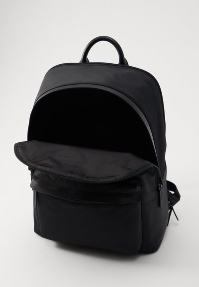 Mochila negra hecha de un tejido liso con una parte superior redondeada. Presenta un bolsillo frontal con cremallera, un compartimento principal amplio y un asa resistente.