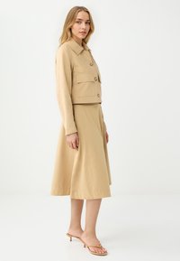 Veste cropped beige avec deux poches avant, associée à une jupe midi fluide beige. Tissu lisse et léger ; design minimaliste.