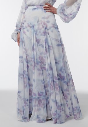 Persona con una falda larga y fluida de tejido translúcido y estampado acuarela en tonos azules, morados y blancos, con la mano apoyada en la cadera.