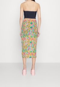 Haut en denim sans bretelles associé à une jupe midi fleurie avec des motifs roses, jaunes et verts, complété par des chaussures roses à talons blocs.