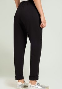 Pantaloni neri a vita elastica con una vestibilità ampia, caratterizzati da orli arrotolati. Tessuto liscio e morbido con una leggera lucentezza. Abbinati a sneakers metalliche.