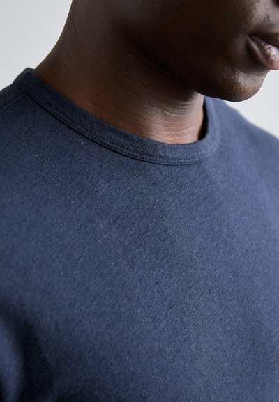 T-shirt en coton bleu marine avec un col rond, tissu texturé et manches courtes, mettant en avant un gros plan de la zone du col.