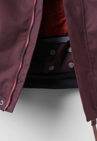 Bordeaux jack met een gestructureerde buitenkant, rode rits en drukknoopsluitingen. Interieur in oranje, met een gestreepte voering.