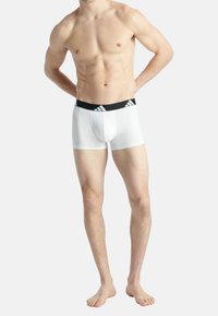 Vita boxertrosor med en svart elastisk midja som har tre vita ränder. Slät textur och kroppsnära design.